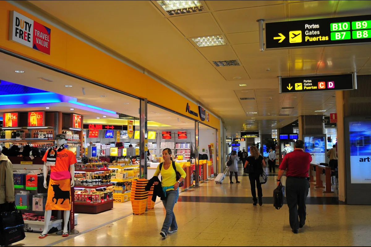 Reisende in einem Flughafenterminal unter einer Anzeigetafel mit Gate-Hinweisen