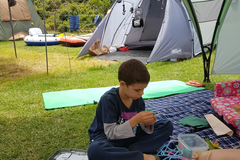 Kind beim Basteln unter einem Vorzelt, dahinter mehrere Campingzelte